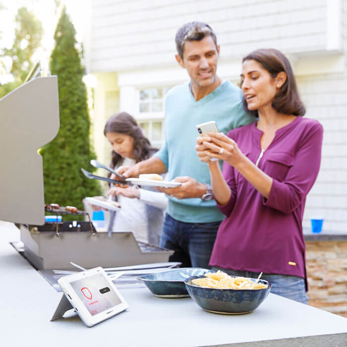 family barbecue with tablet on table with home security app
