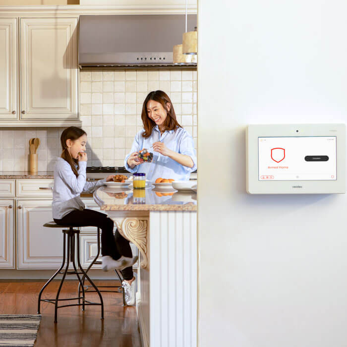 home security panel on wall while mother and daughter happy in the kitchen