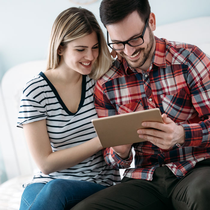 man and woman sitting on couch looking at tablet
