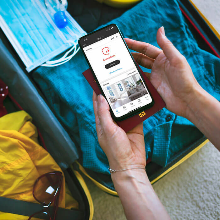 hands holding phone with home security app while packing suitcase