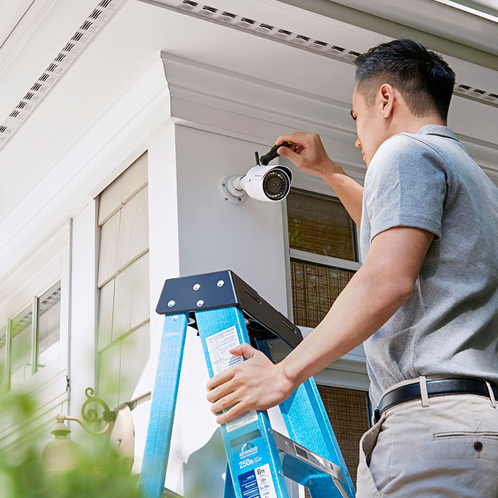 man on ladder installing camera to house